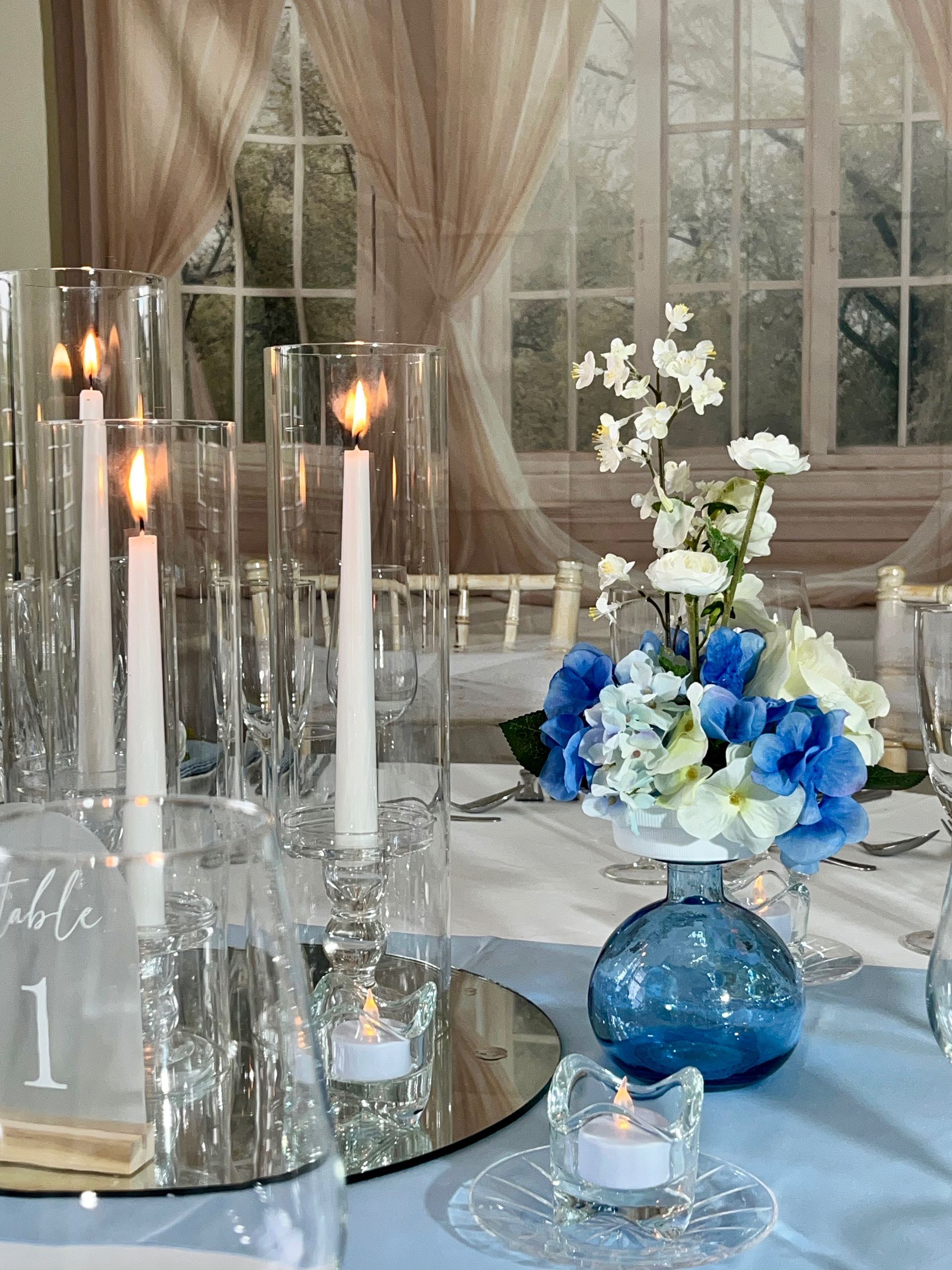 Blue-and-white floral centerpiece with candles on a mirrored table at a formal event