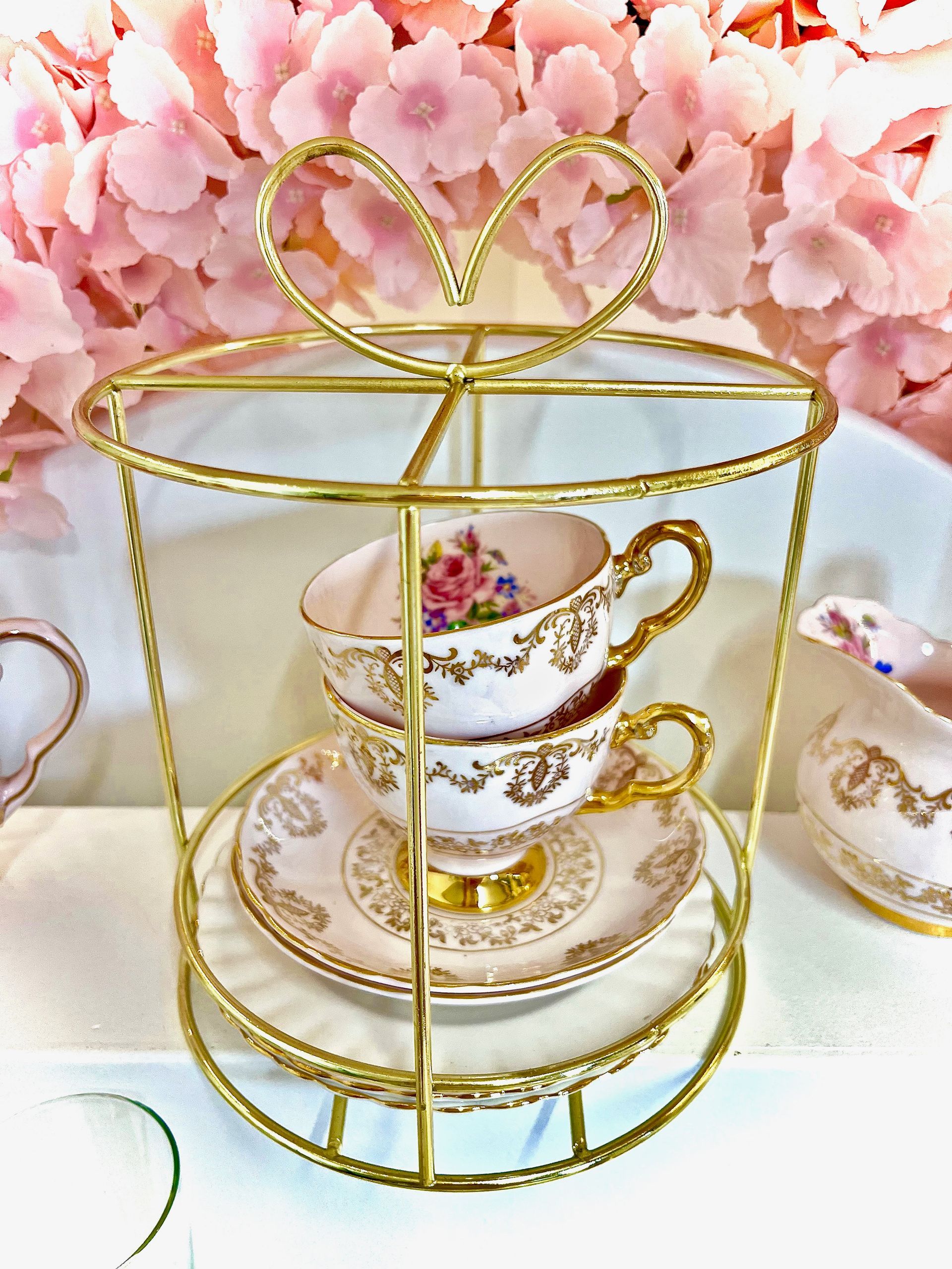 Gold teacup stand with stacked floral china cups and saucers against pink blossoms