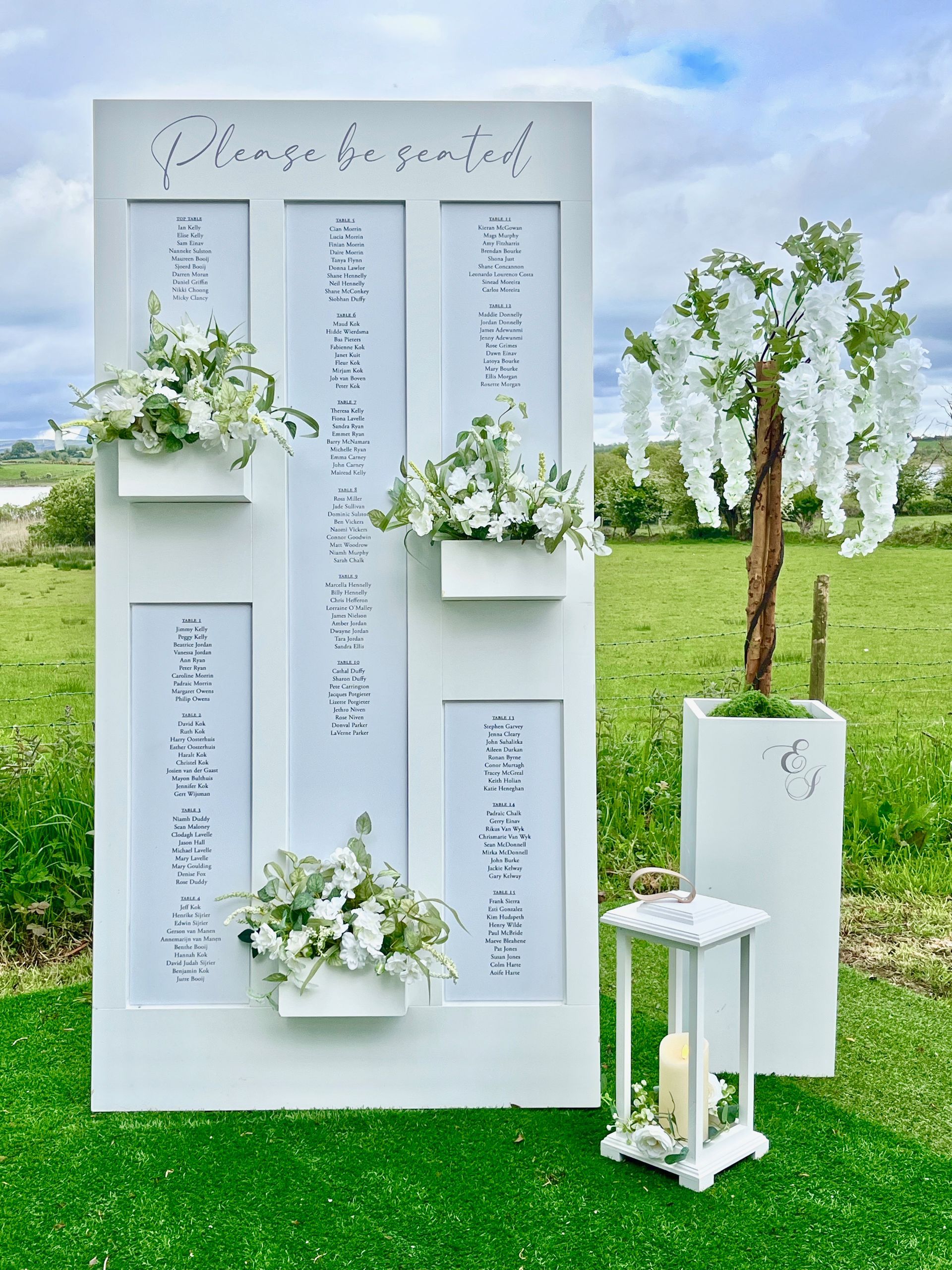 White wedding seating chart boards with floral arrangements on grass outdoors