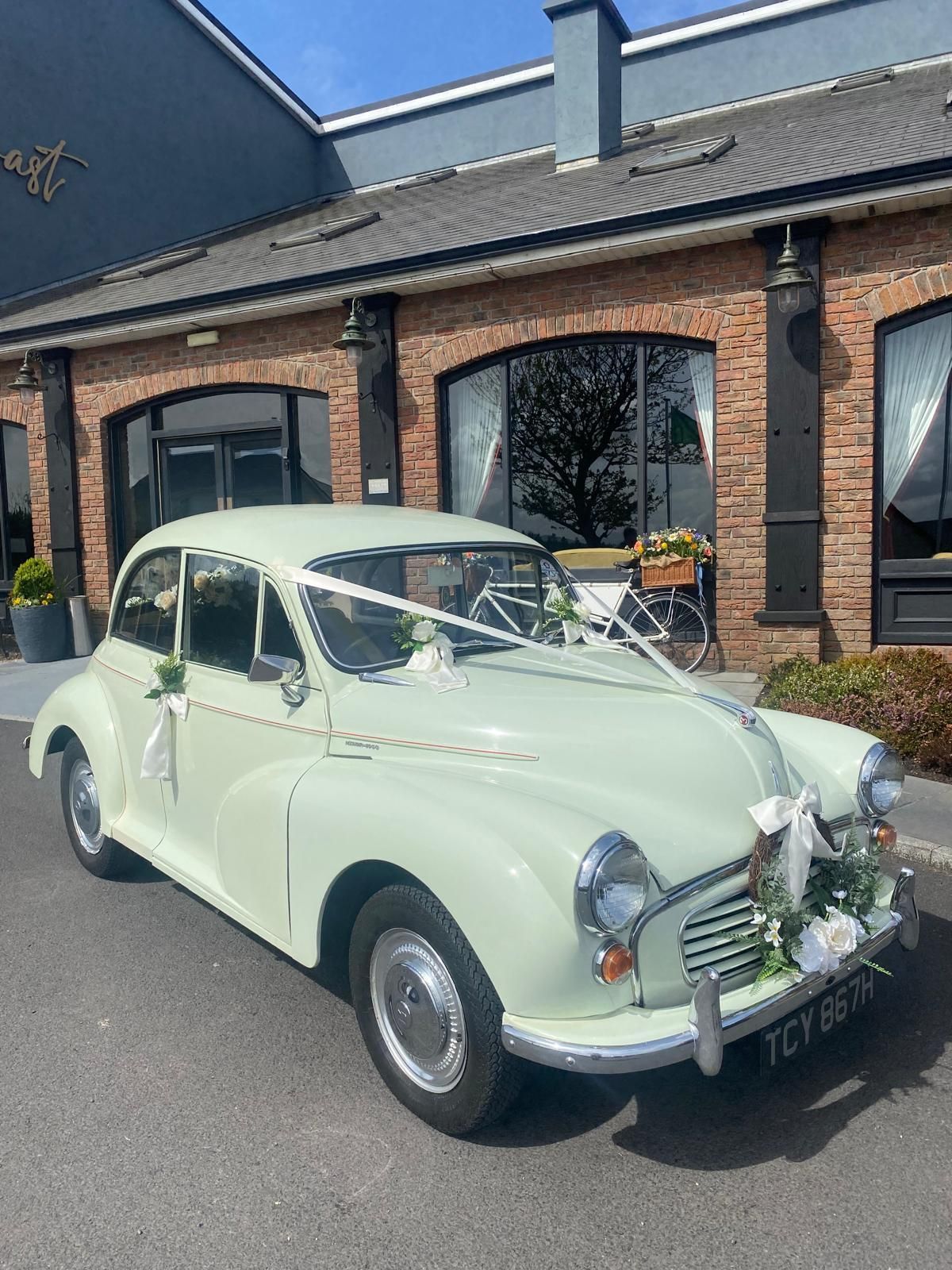 Mint-green vintage car parked outside a brick building with dark windows.