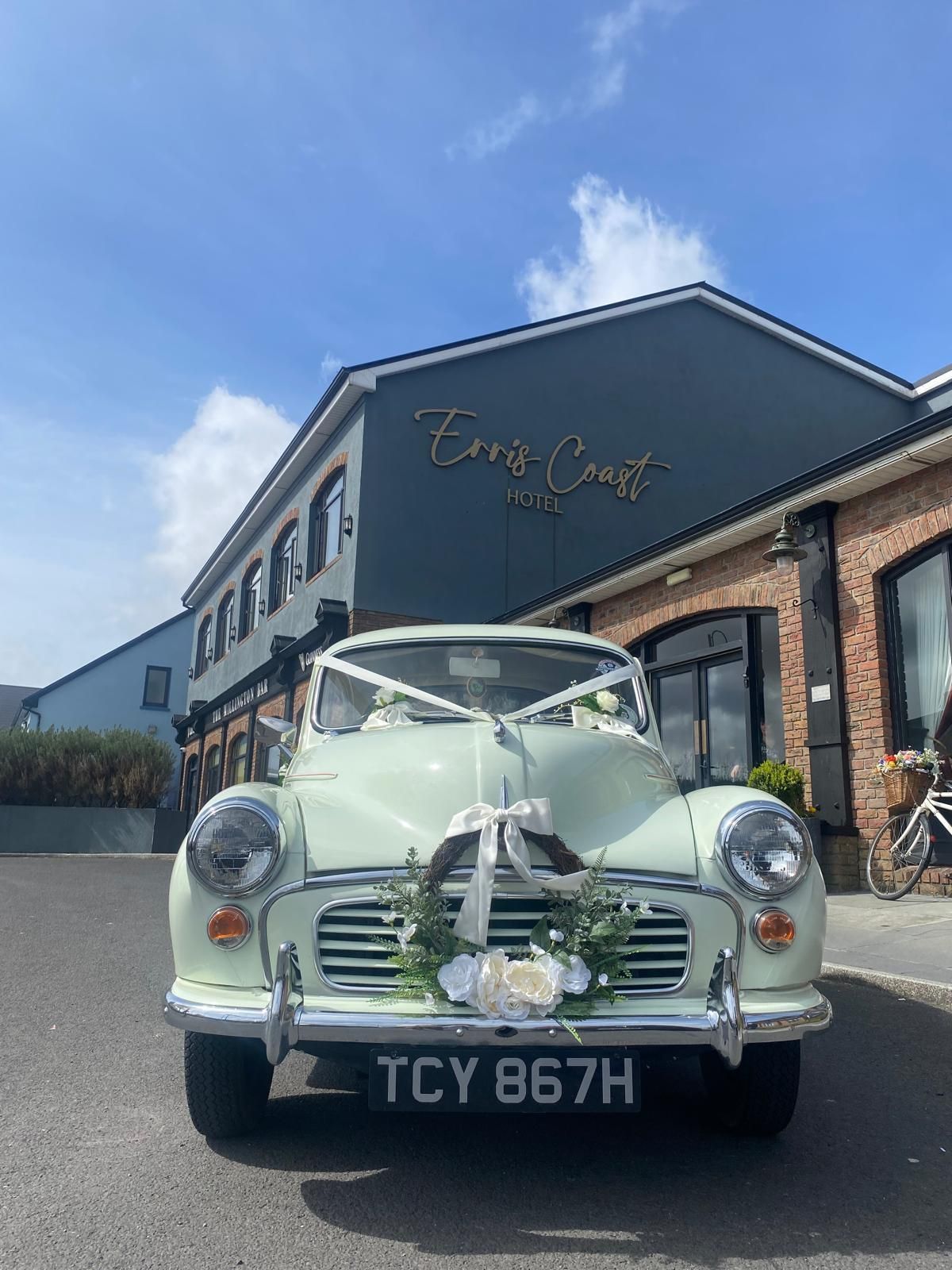 Vintage pale green car parked outside a brick building under a blue sky.