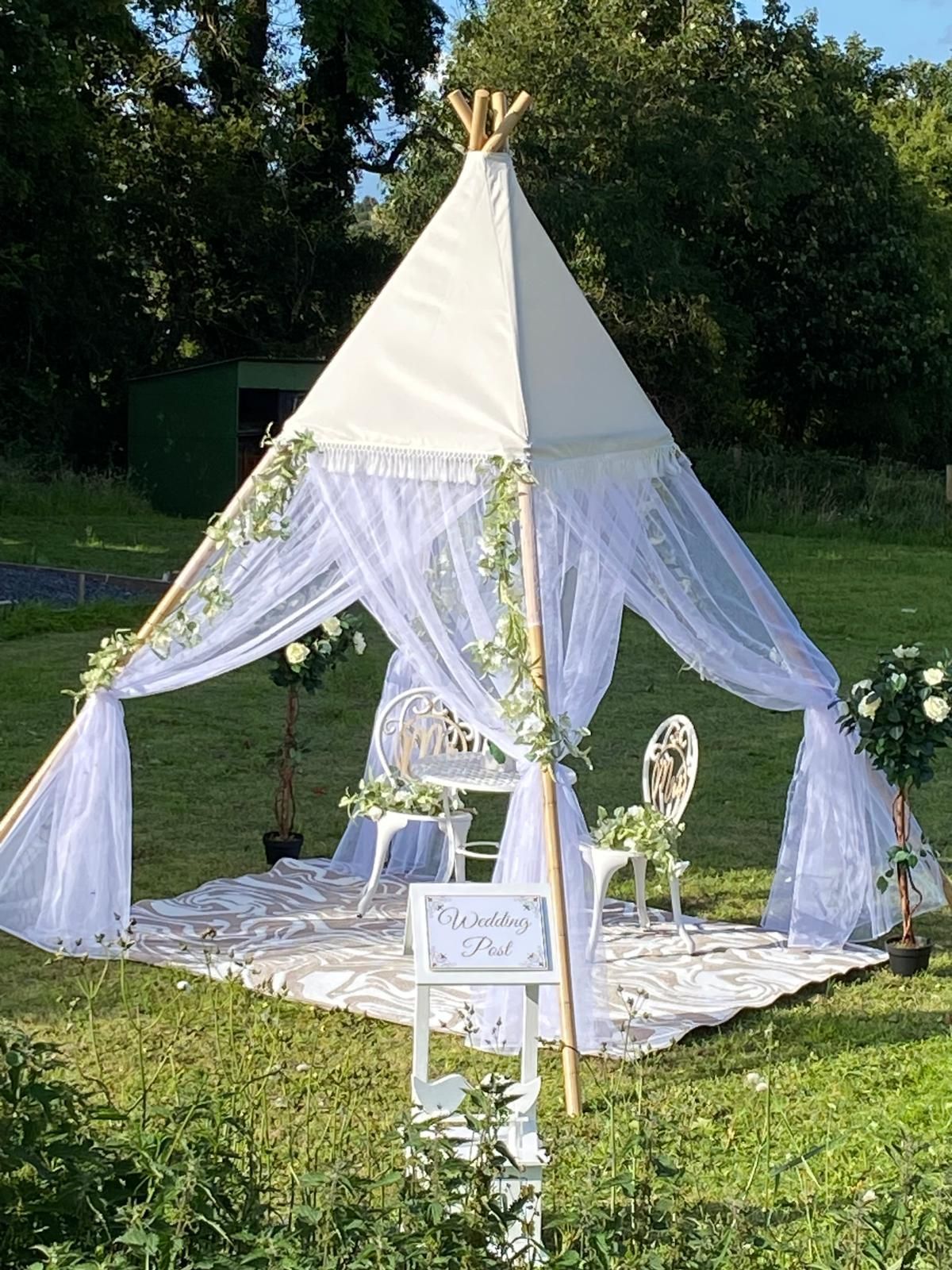 White outdoor wedding gazebo with draped sheer curtains, floral decor, and a sign on a lawn
