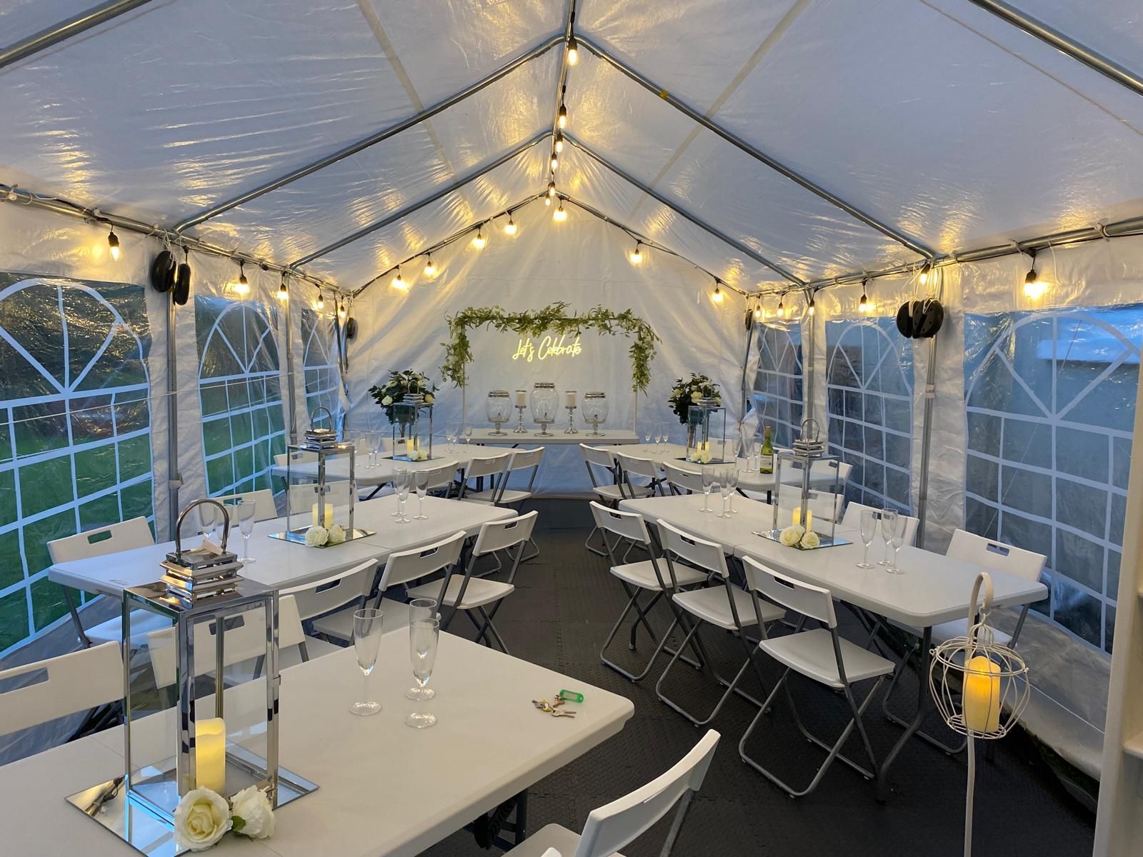 Decorated white event tent with string lights, tables, and chairs set for a celebration