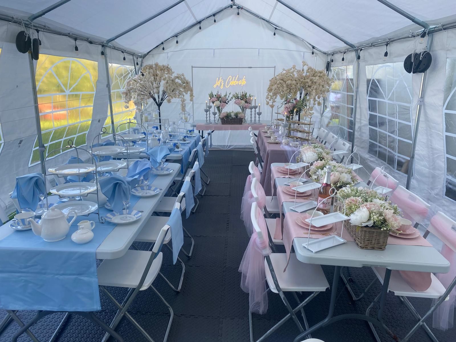 Decorated outdoor tent with long dining tables set for an event, in blue and pink