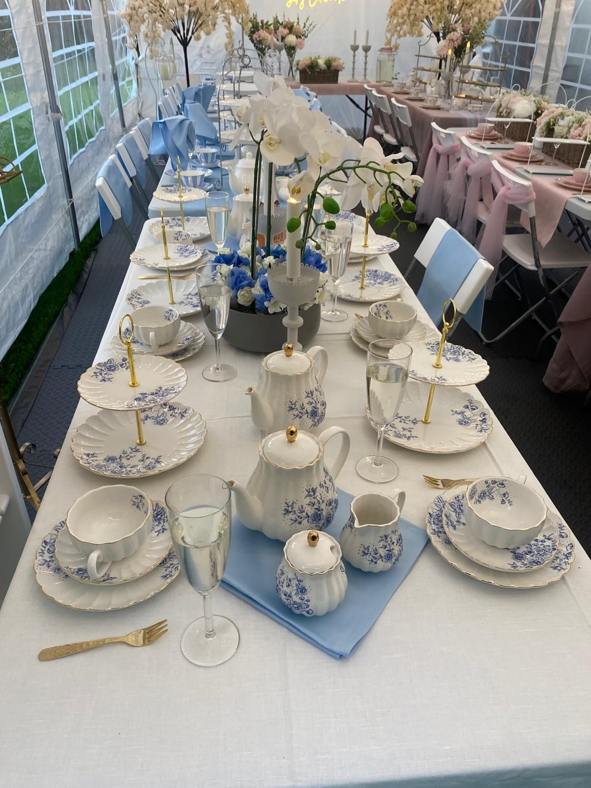 Long banquet table with white-and-blue china, teacups, and floral centerpieces in a tented setting