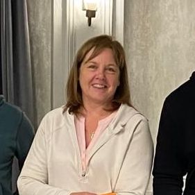 Smiling woman in a light jacket standing indoors beside others