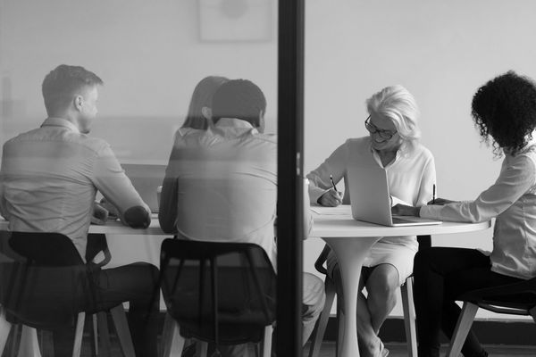 A group of people are sitting around a table with laptops.