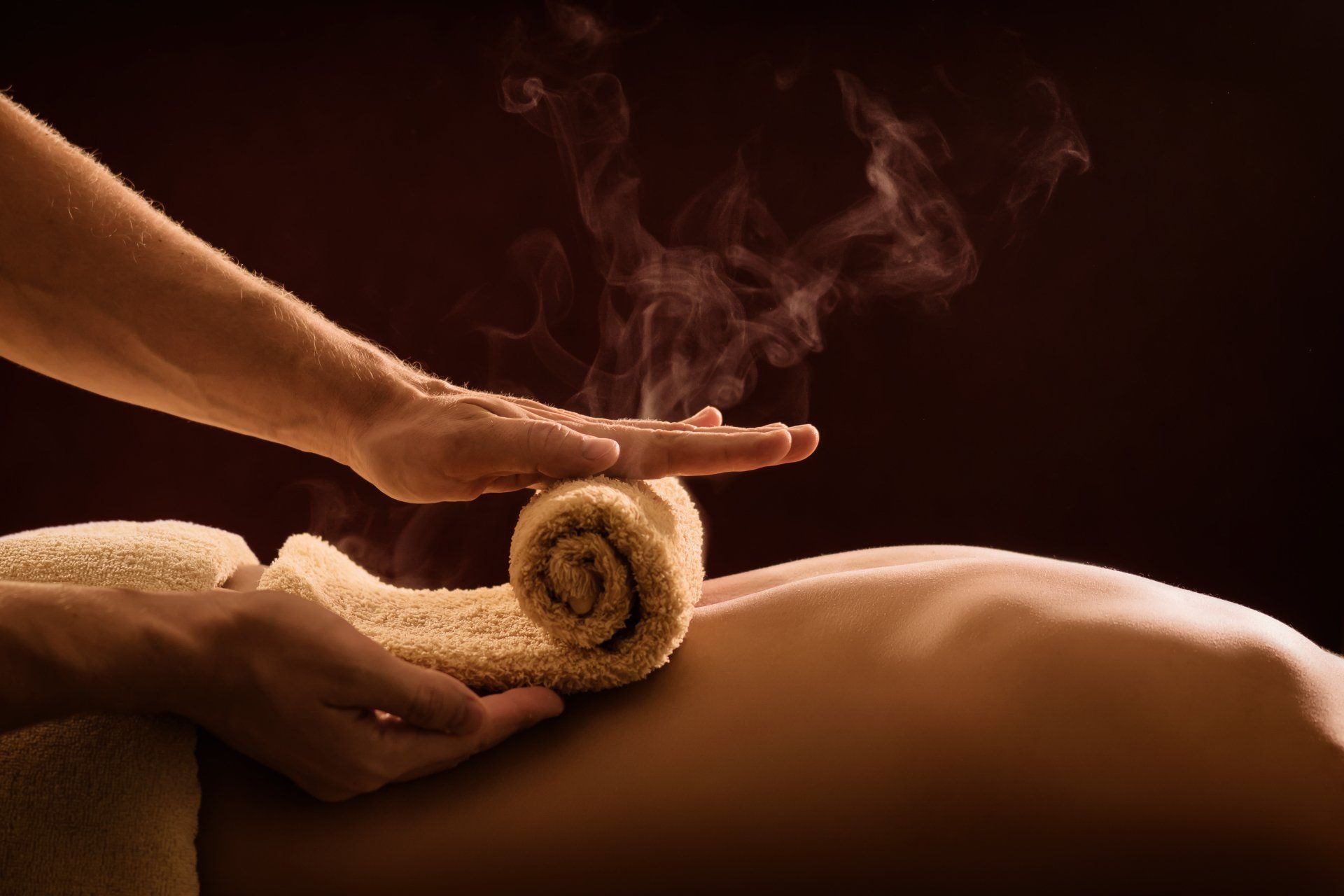 A professional therapist applies a hot towel on the back of a man