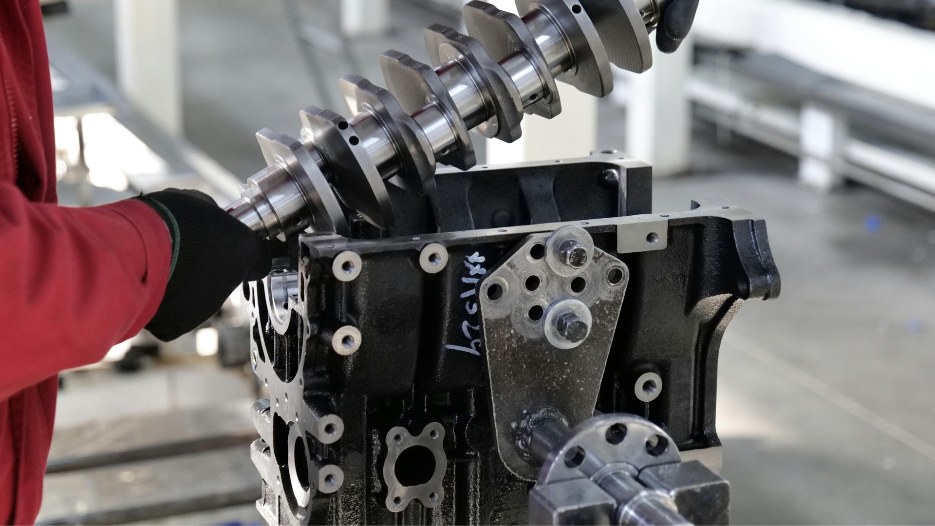 Worker in red gloves inspecting a metal engine block with a drill bit in a workshop