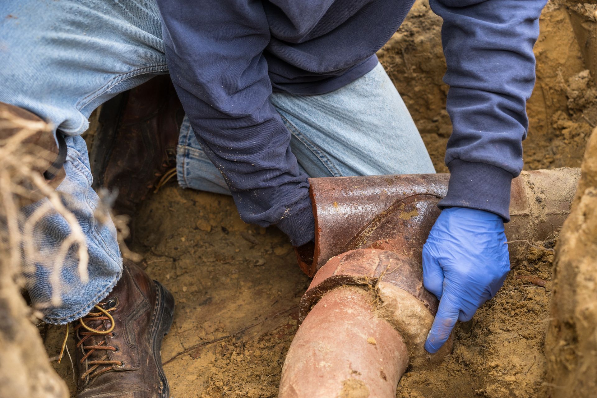 Worker repairing a damaged underground sewer pipe in a trench.