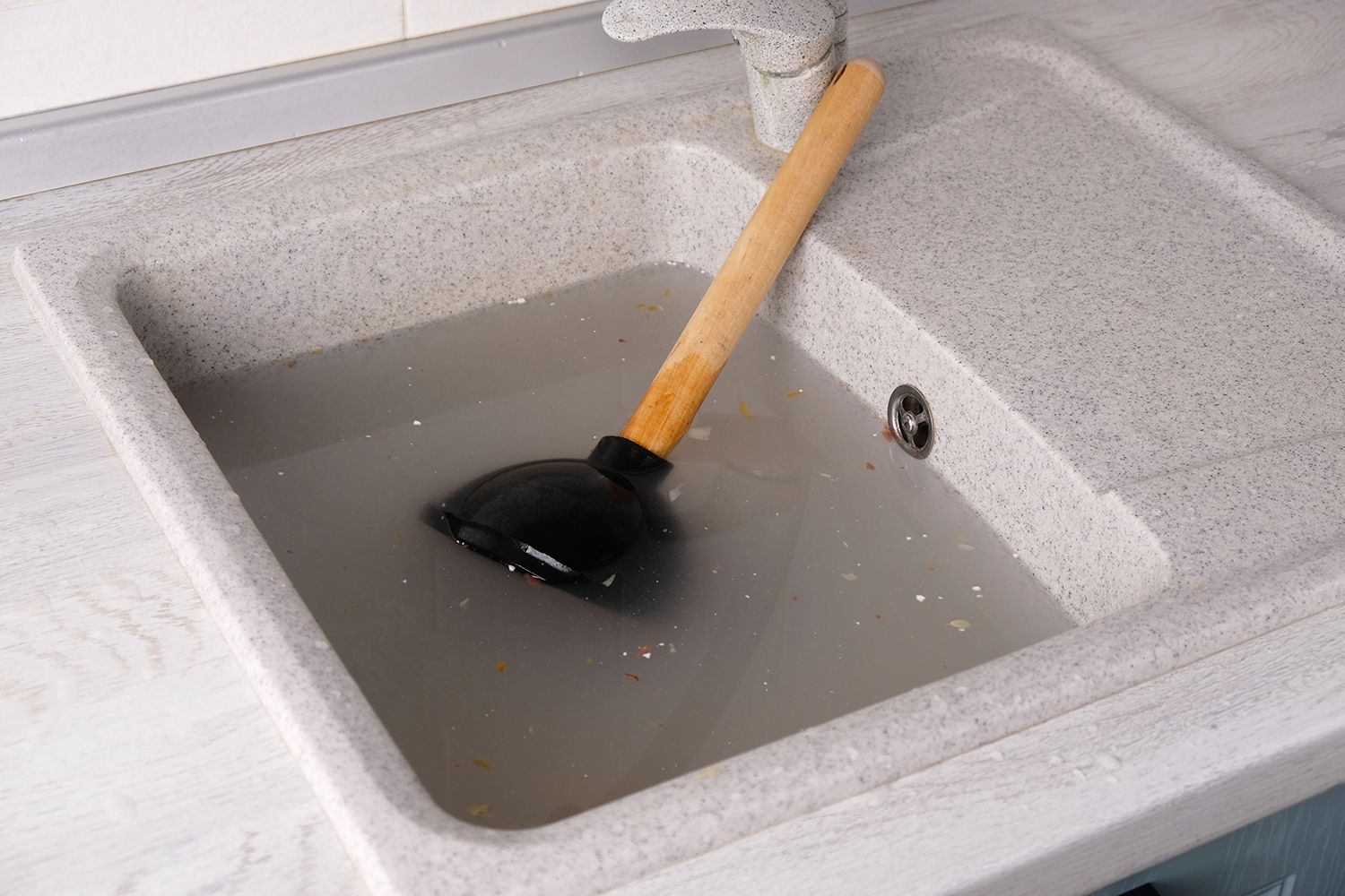 Kitchen sink filled with cloudy water and a plunger resting inside, showing a drainage issue.