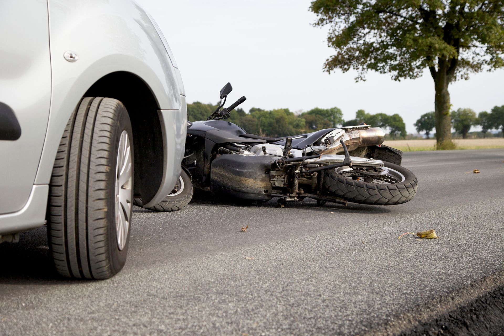A motorcycle has crashed into a car on the side of the road.
