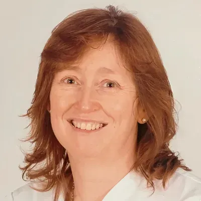 Smiling woman with shoulder-length auburn hair wearing a white top against a plain light background