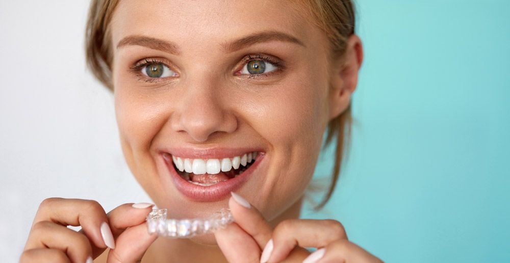 Smiling person holding clear dental aligners against a light blue background