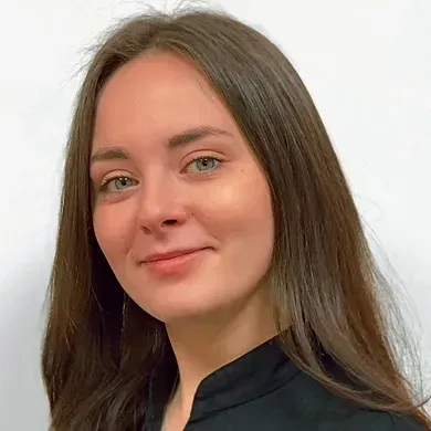 Smiling person with long brown hair in a dark top against a light background