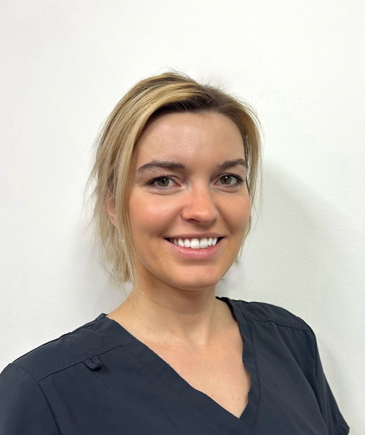 Smiling woman in a navy top against a plain light wall