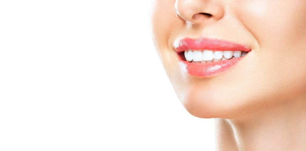 Close-up of a smiling mouth with bright white teeth, a nose ring, and glossy pink lips on a white background