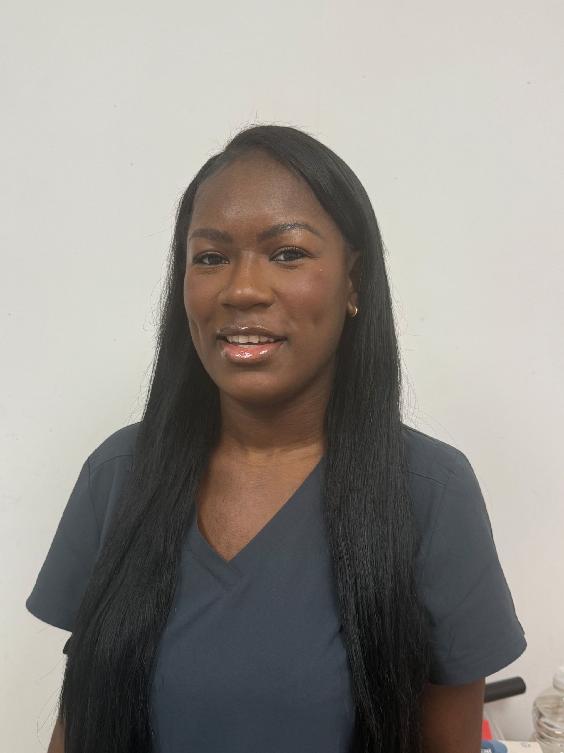 Woman smiling in a dark scrub top against a plain white background