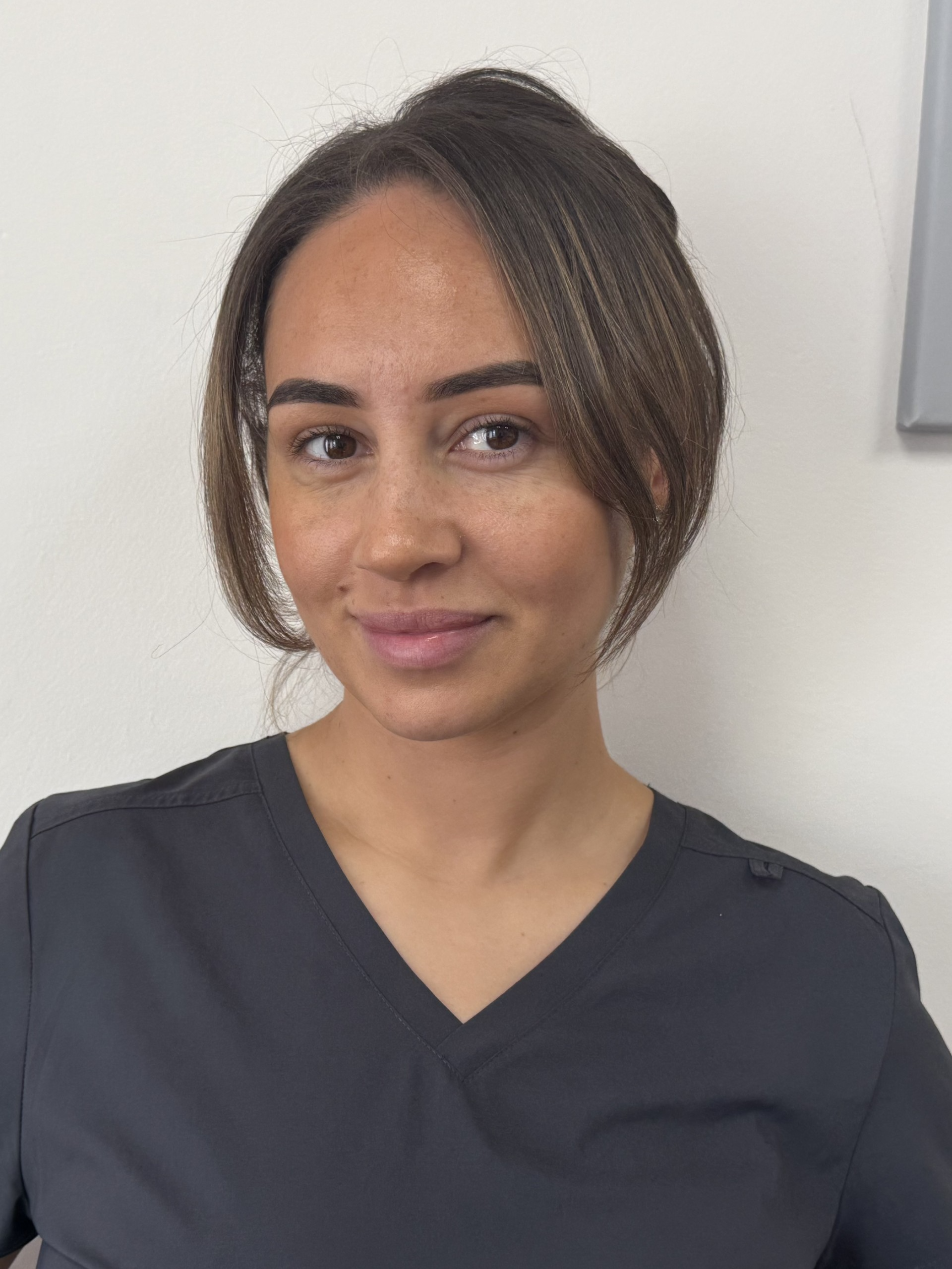 Portrait of a person in dark gray scrubs, smiling against a light background