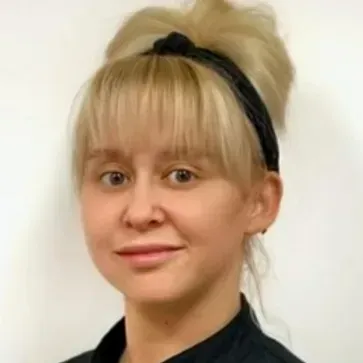 Portrait of a woman with blonde hair in a bun and black headband, smiling against a plain background