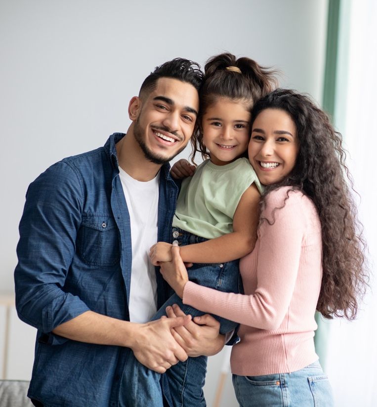 Three people smiling and hugging indoors, with a child in the center.
