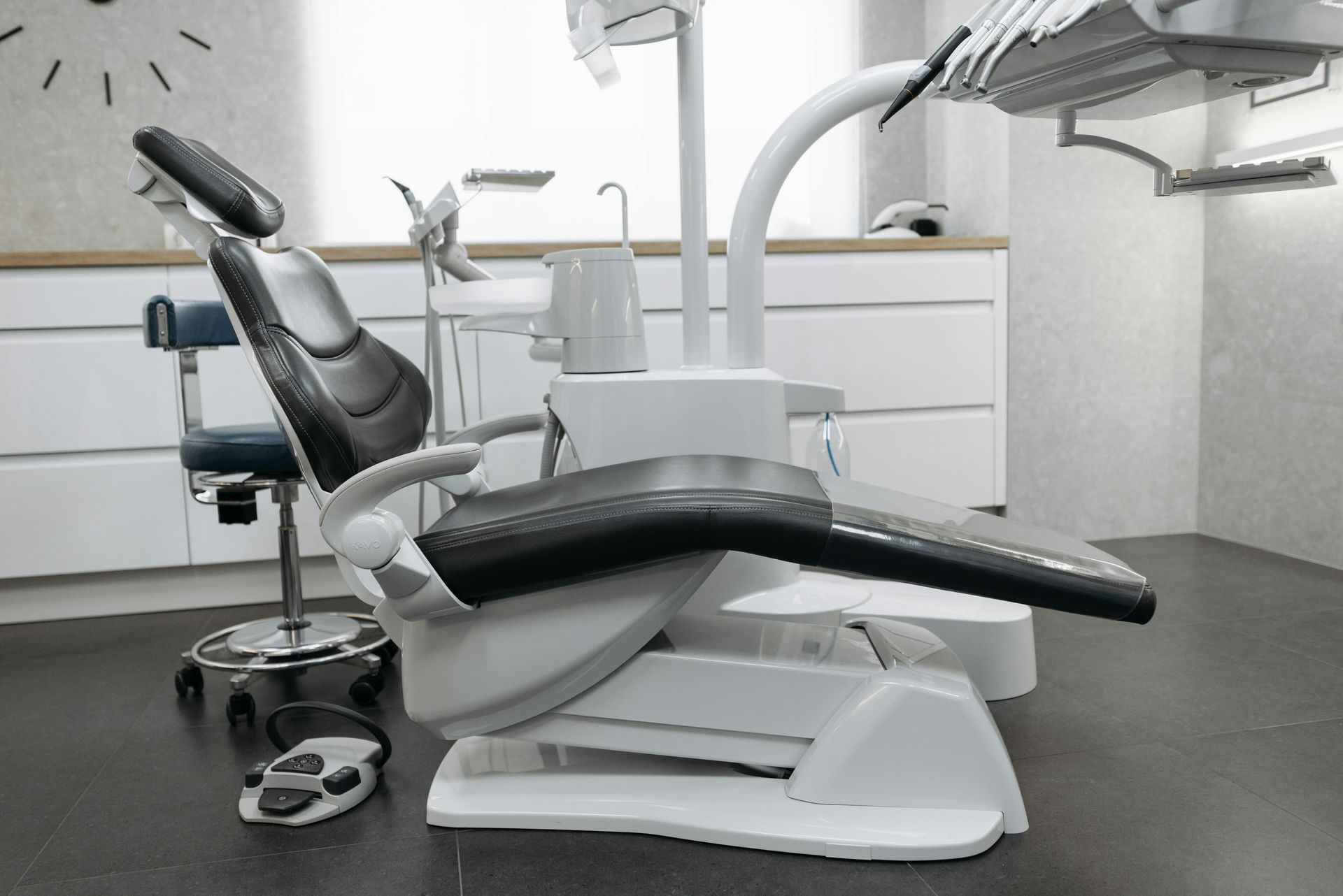 Modern dental office with an empty black reclining chair and dental tools beside a sink and drawers