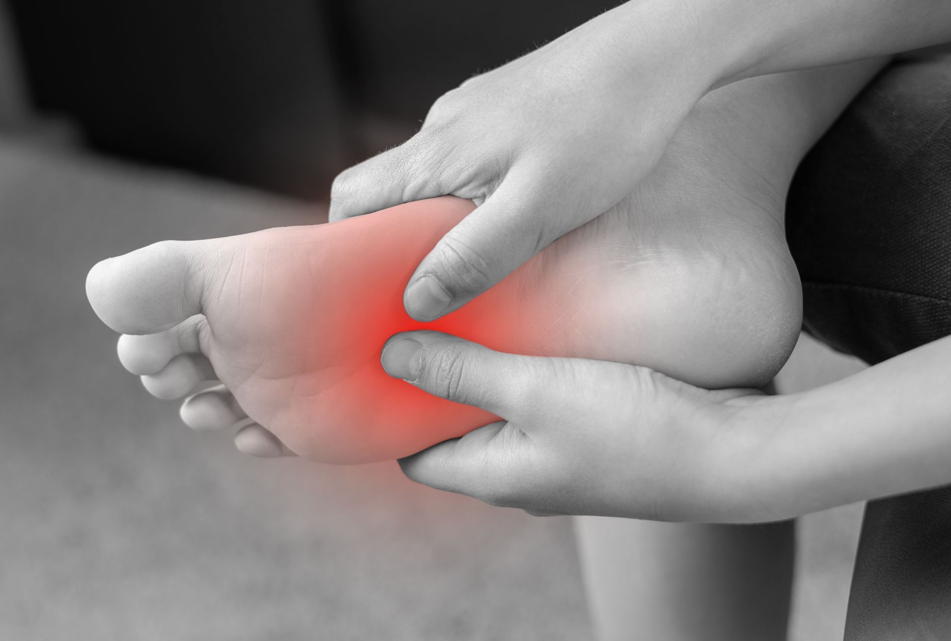 Person holding their foot, the sole highlighted in red indicating pain.