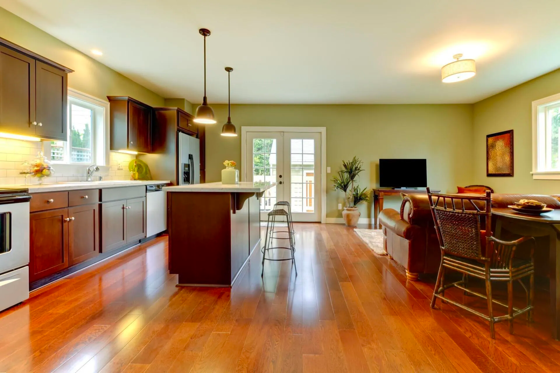 Open-concept living space with kitchen and living room. Brown cabinets, wood floors, olive green walls, and a leather sofa.