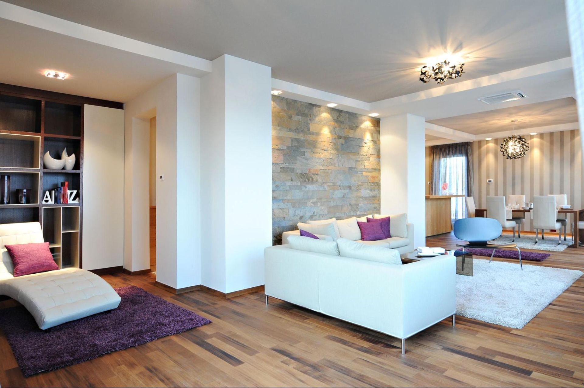 Modern living room with white sofa, stone accent wall, wooden floors, and dining area.