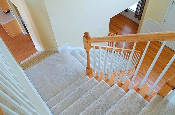 Staircase with light-colored carpet and wooden railing. View from above, leading down.