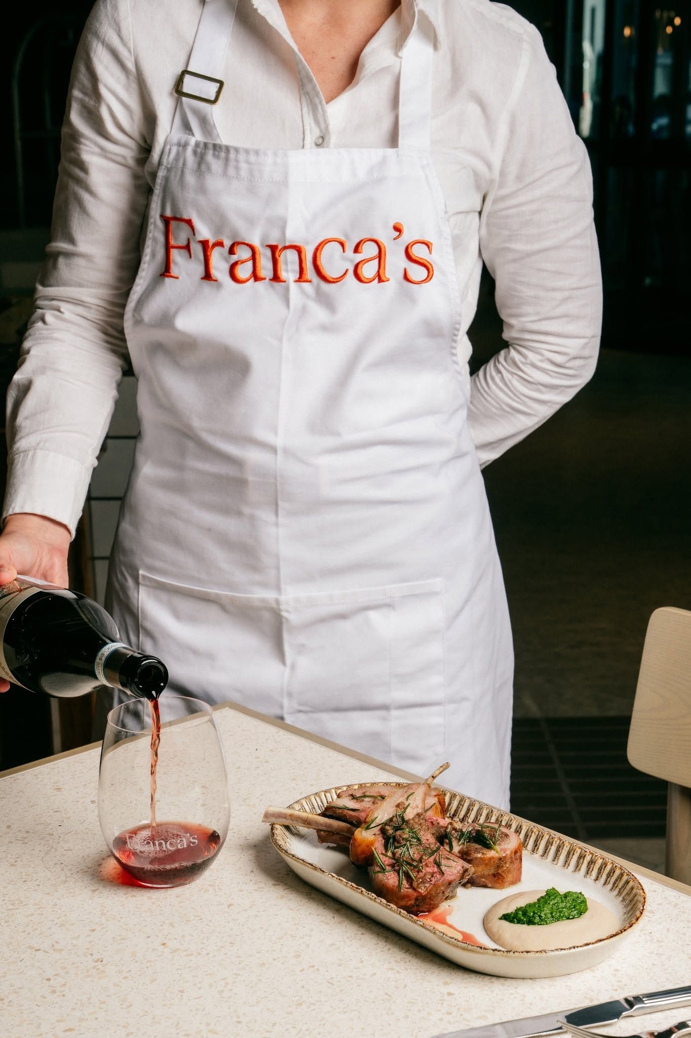 Server pouring red wine beside plated meal at Franca’s restaurant