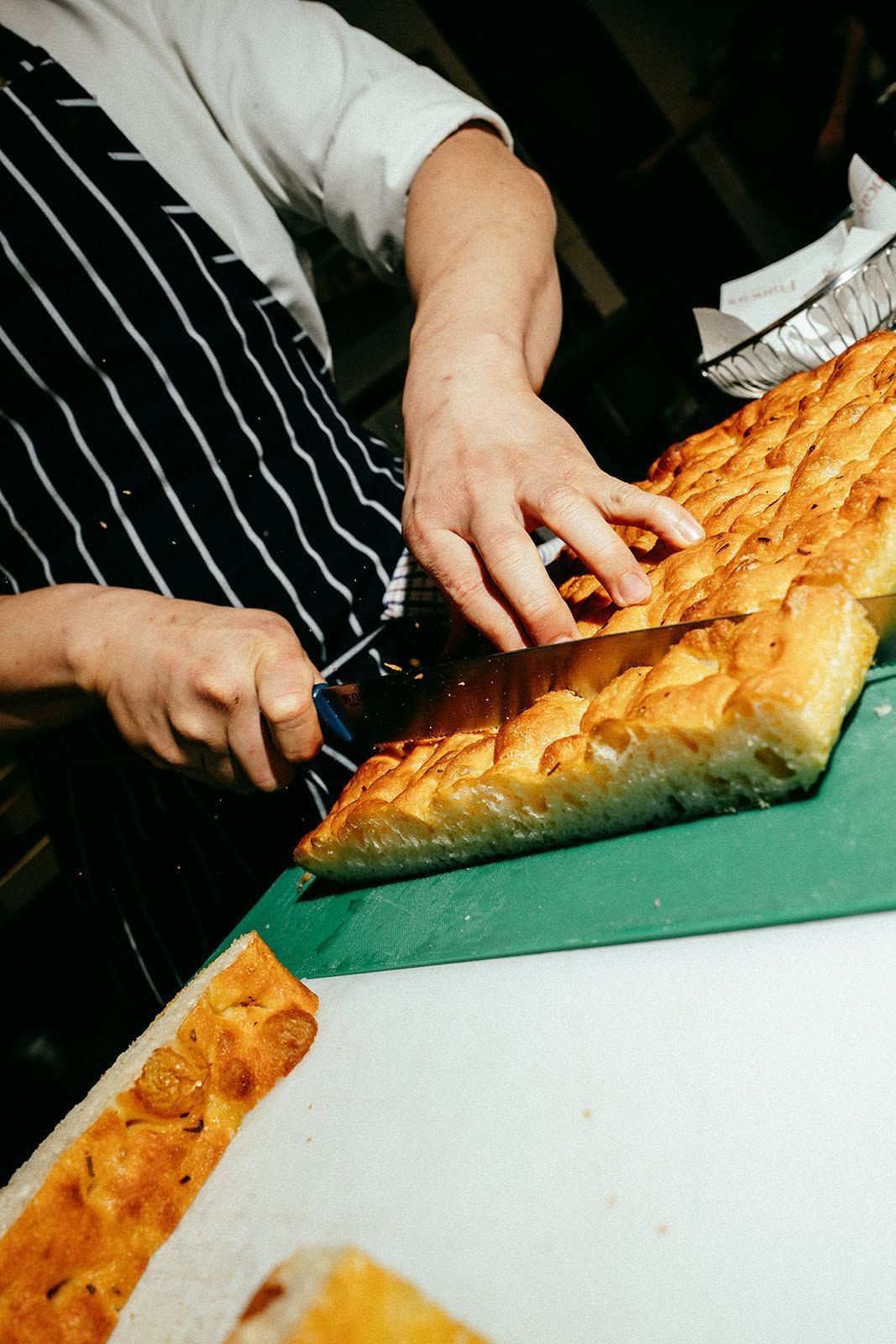 Hands slicing a golden-brown loaf on a green cutting board in a kitchen.