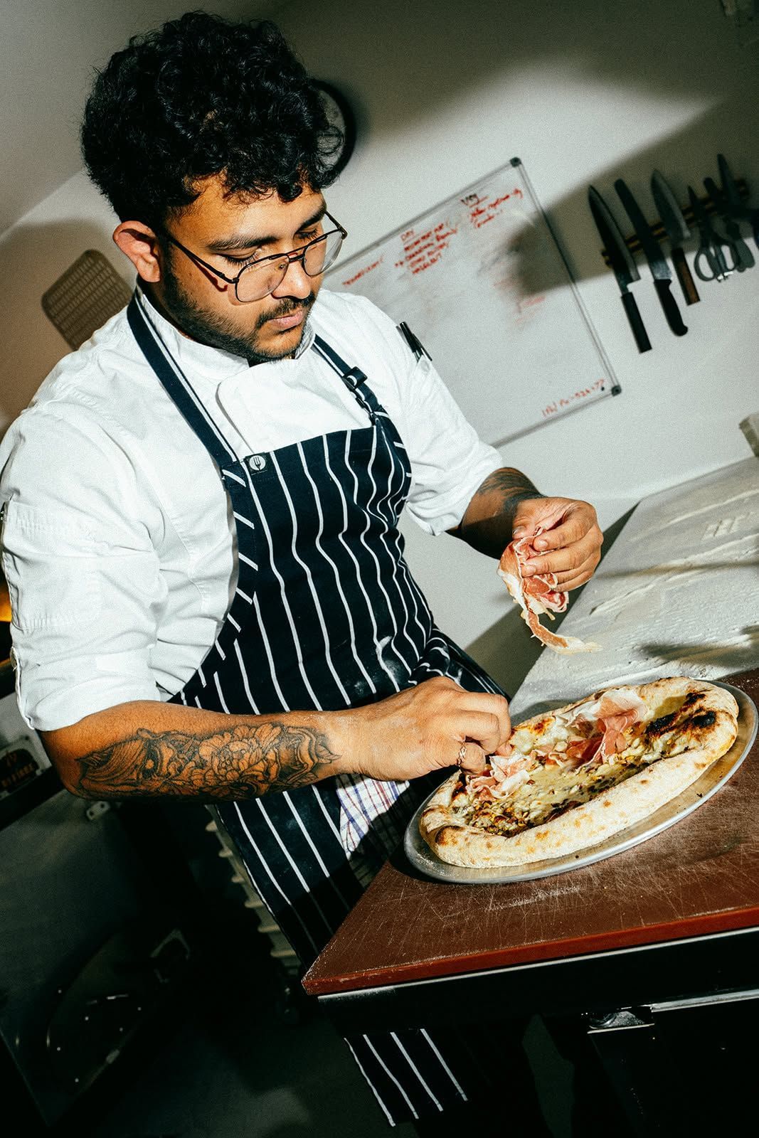 Chef slicing a pizza in a kitchen, wearing a striped apron and white shirt
