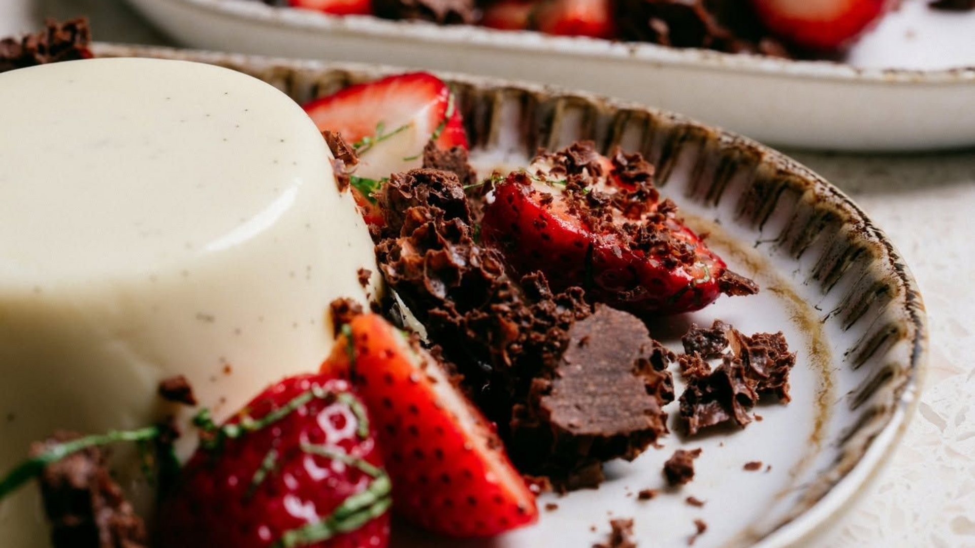 Chocolate dessert with strawberries beside a white panna cotta on a plate