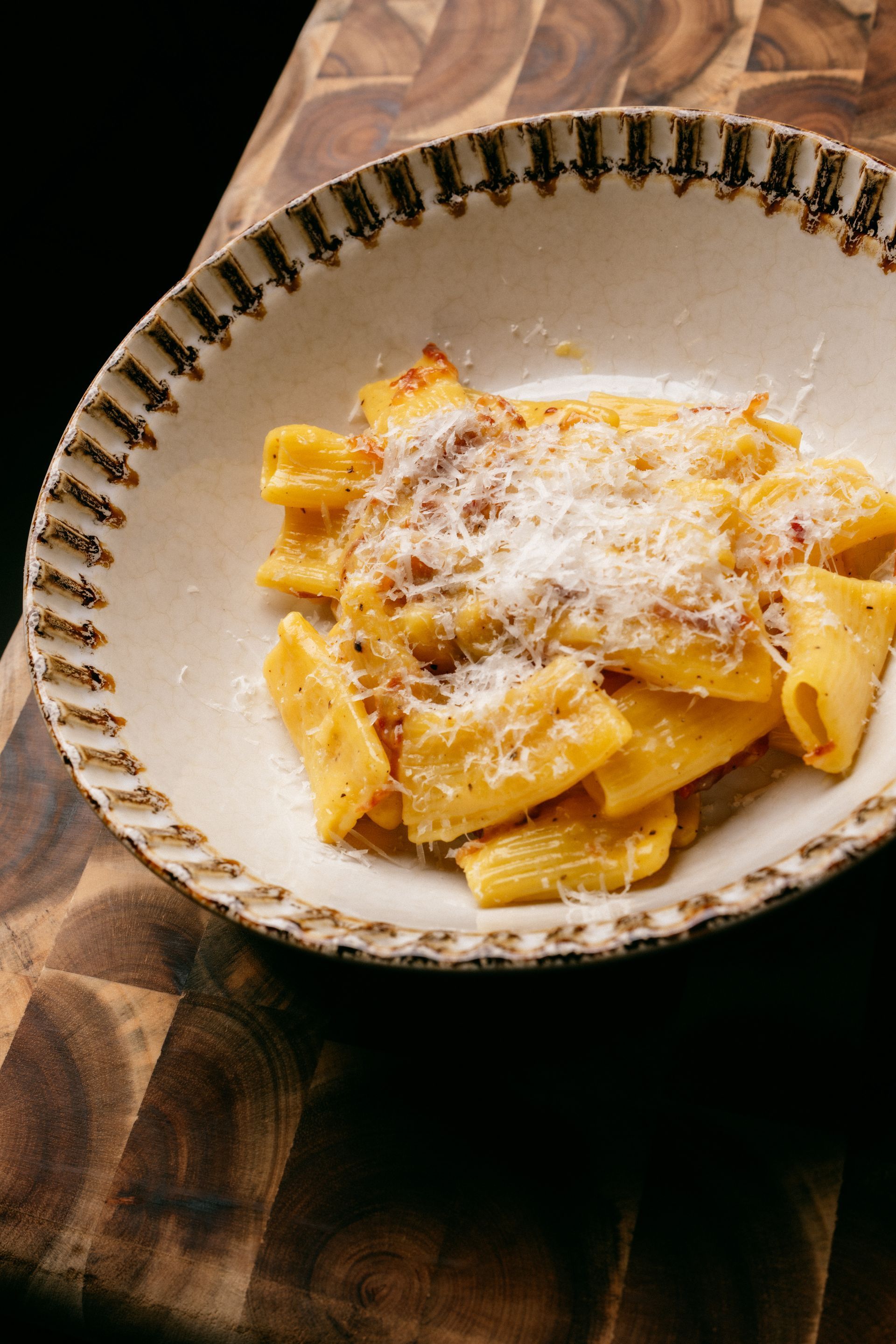 Pasta in a white bowl topped with grated cheese on a wooden table.