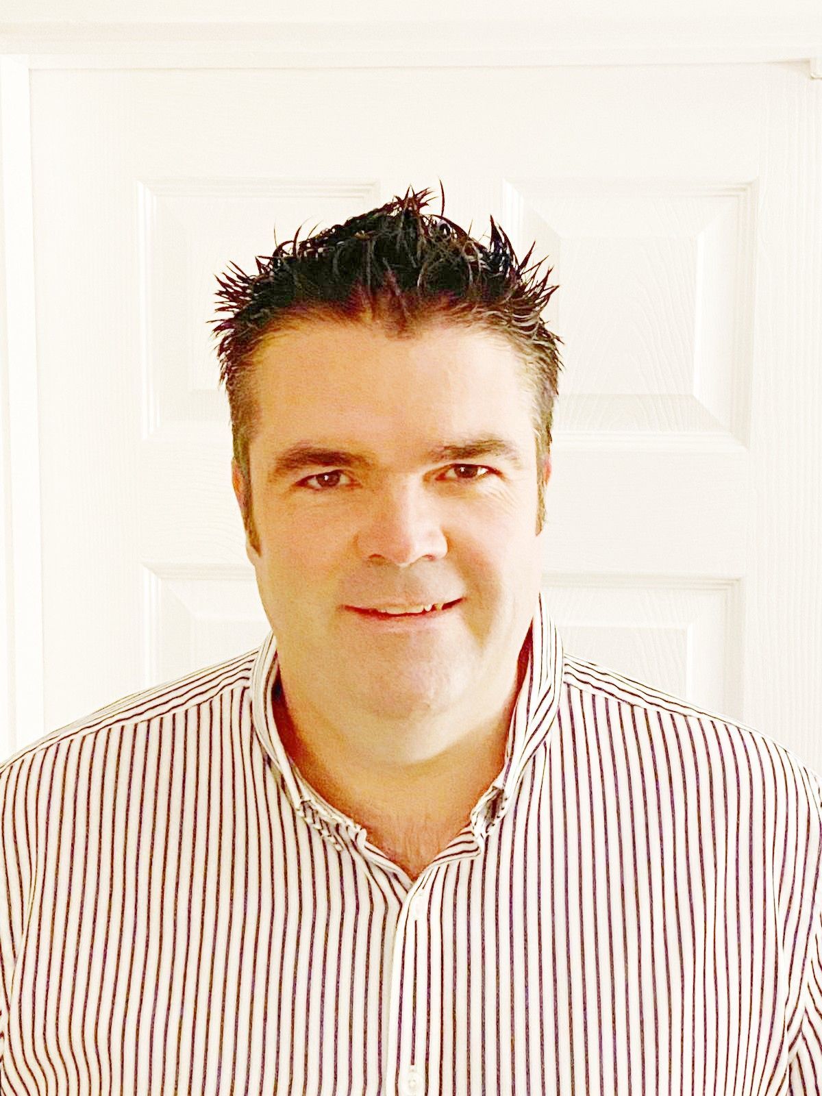 Matt in a striped shirt is smiling in front of a white door.