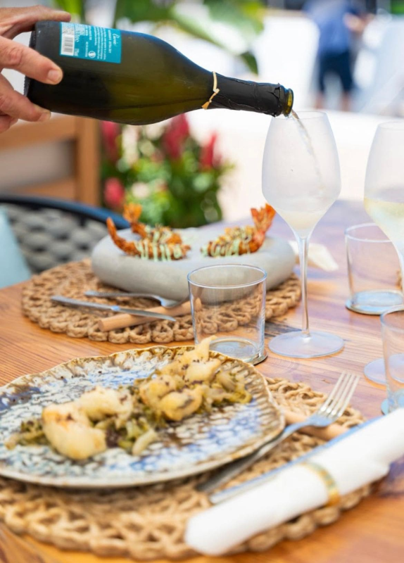 Il vino viene versato in un bicchiere accanto a frutti di mare serviti su un tavolo di vimini all'aperto.