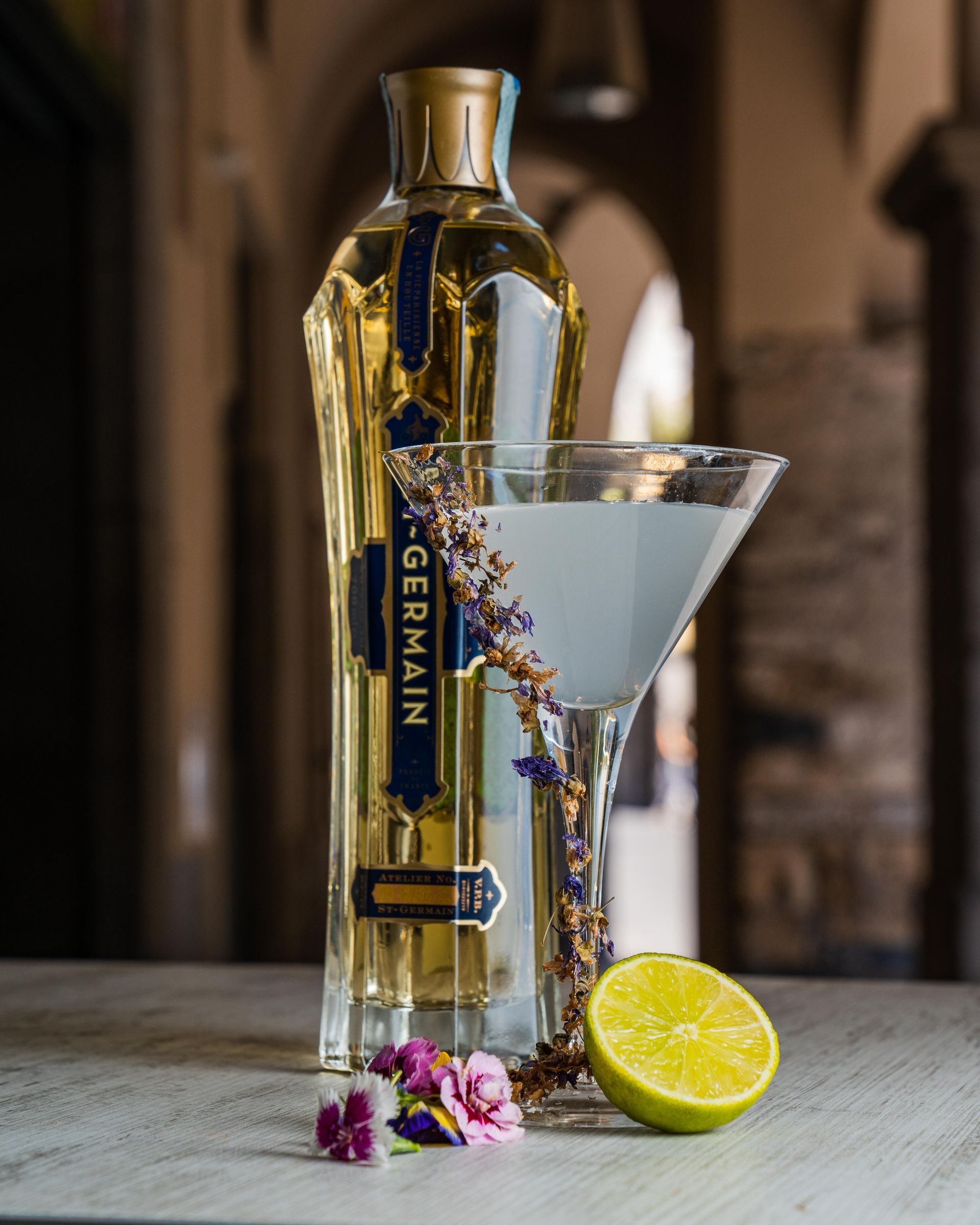 Bottiglia da cocktail e bicchiere da martini con spicchio di lime e fiori su un tavolo