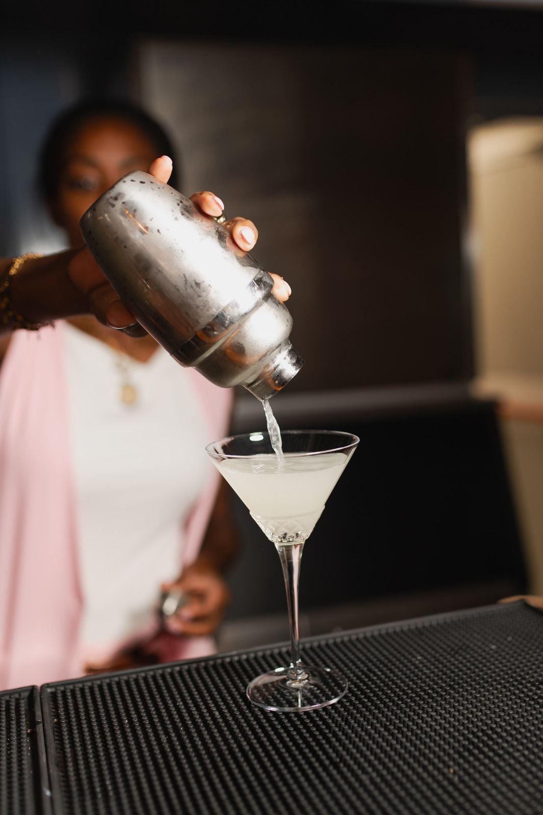 Un barista filtra un cocktail bianco in un bicchiere da martini al bancone di un bar.
