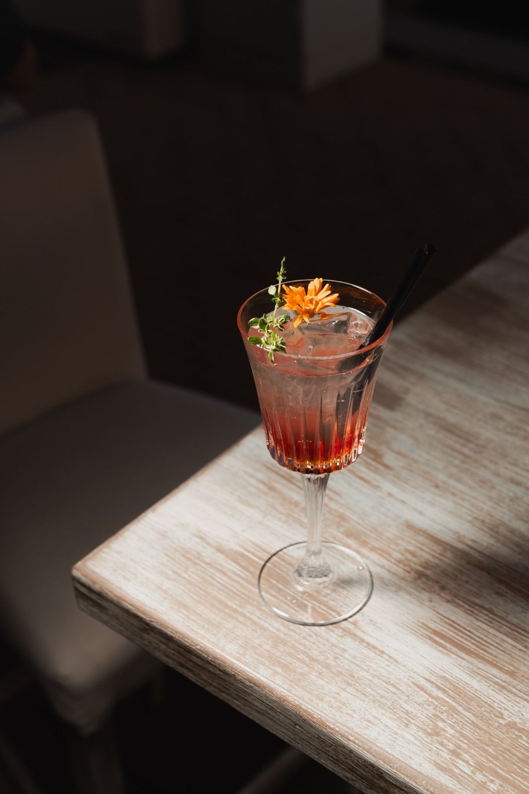 Cocktail con guarnizione di agrumi e cannuccia su un tavolino di legno in penombra