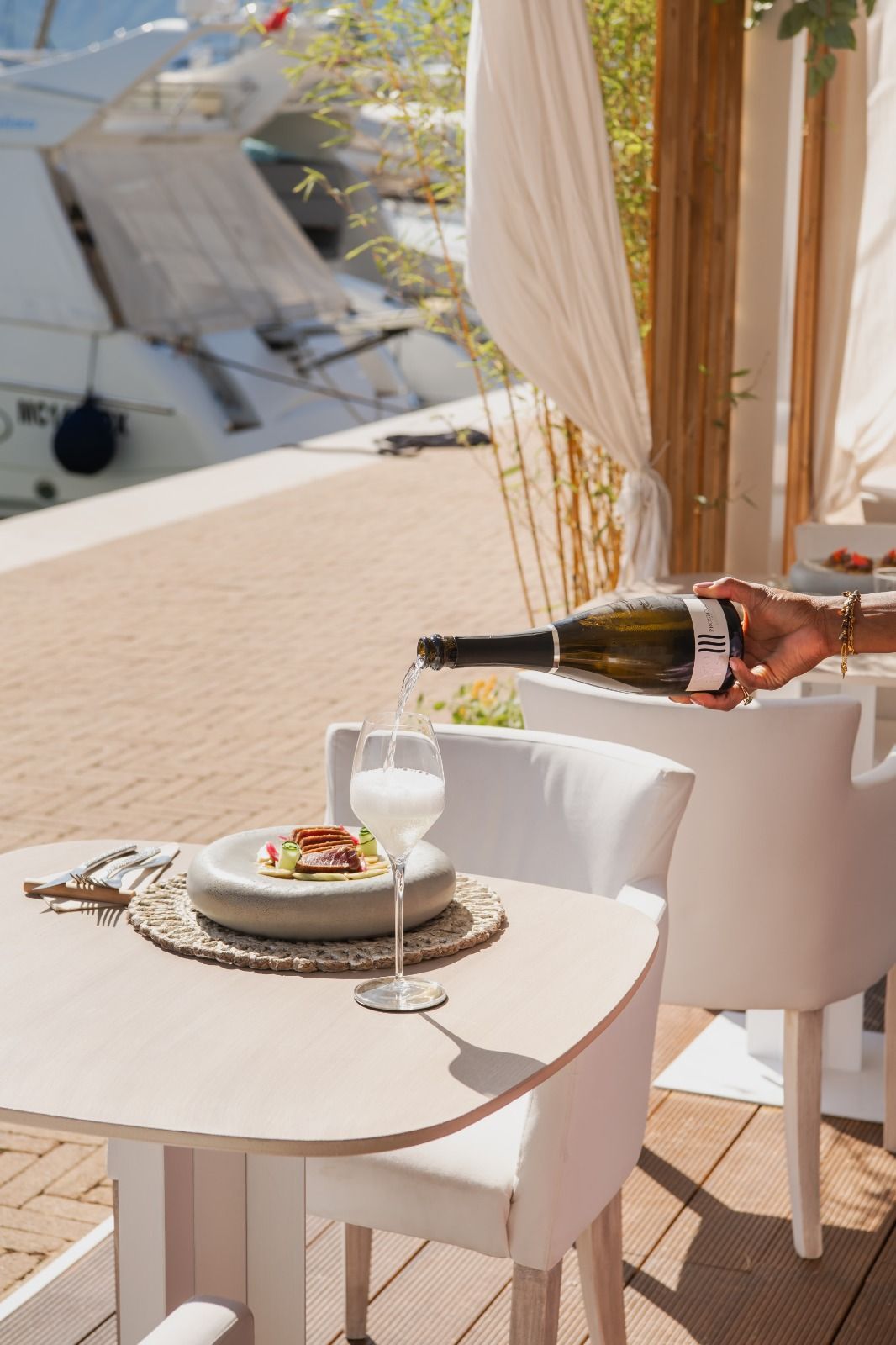Il vino viene versato accanto a un tavolo apparecchiato con un dessert su un balcone soleggiato con vista sull'acqua.