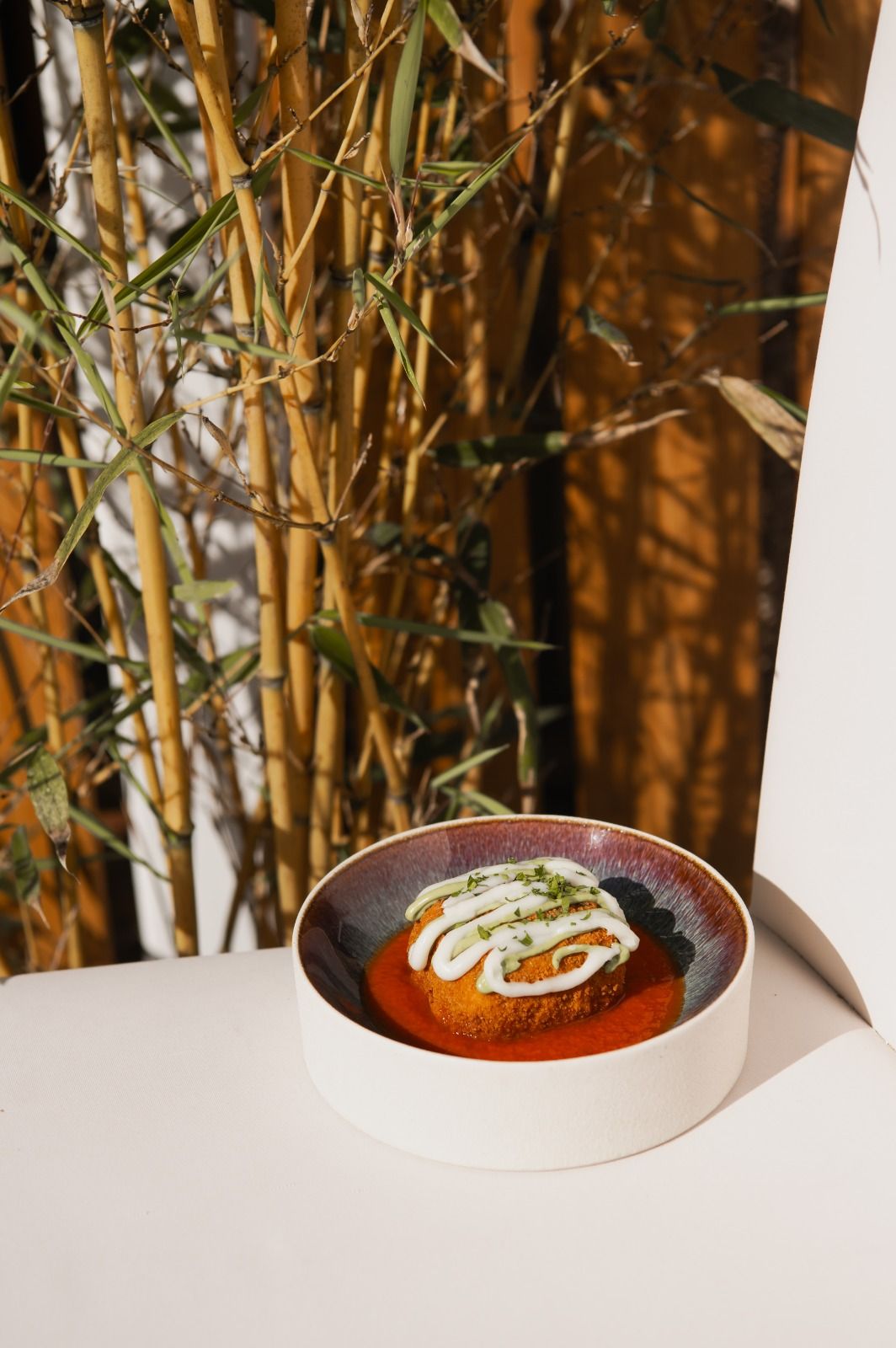 Su un tavolo, con una ciotola bianca di zuppa rossa guarnita con panna ed erbe aromatiche e decorazioni in bambù sullo sfondo, si trova un elemento decorativo.