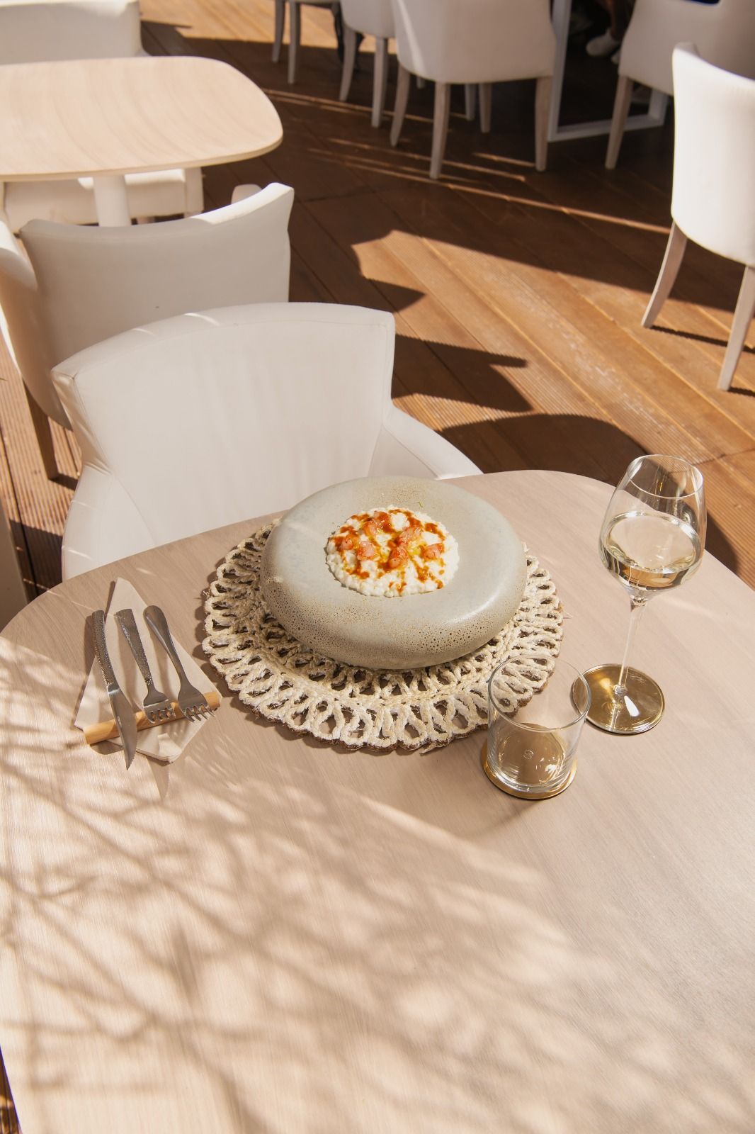 Tavolo da ristorante con dessert al piatto, calice da vino e posate, illuminato da una calda luce solare.
