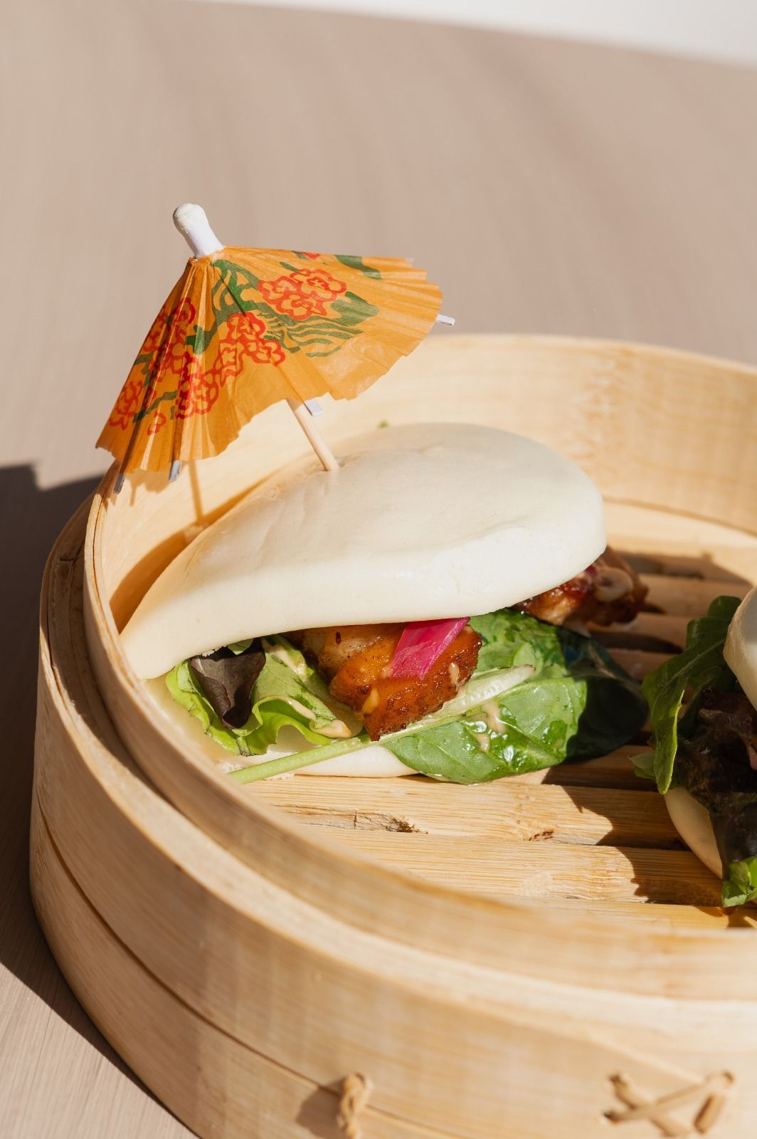 Panino al vapore cotto in una vaporiera di bambù, guarnito con un minuscolo ombrellino di carta arancione.