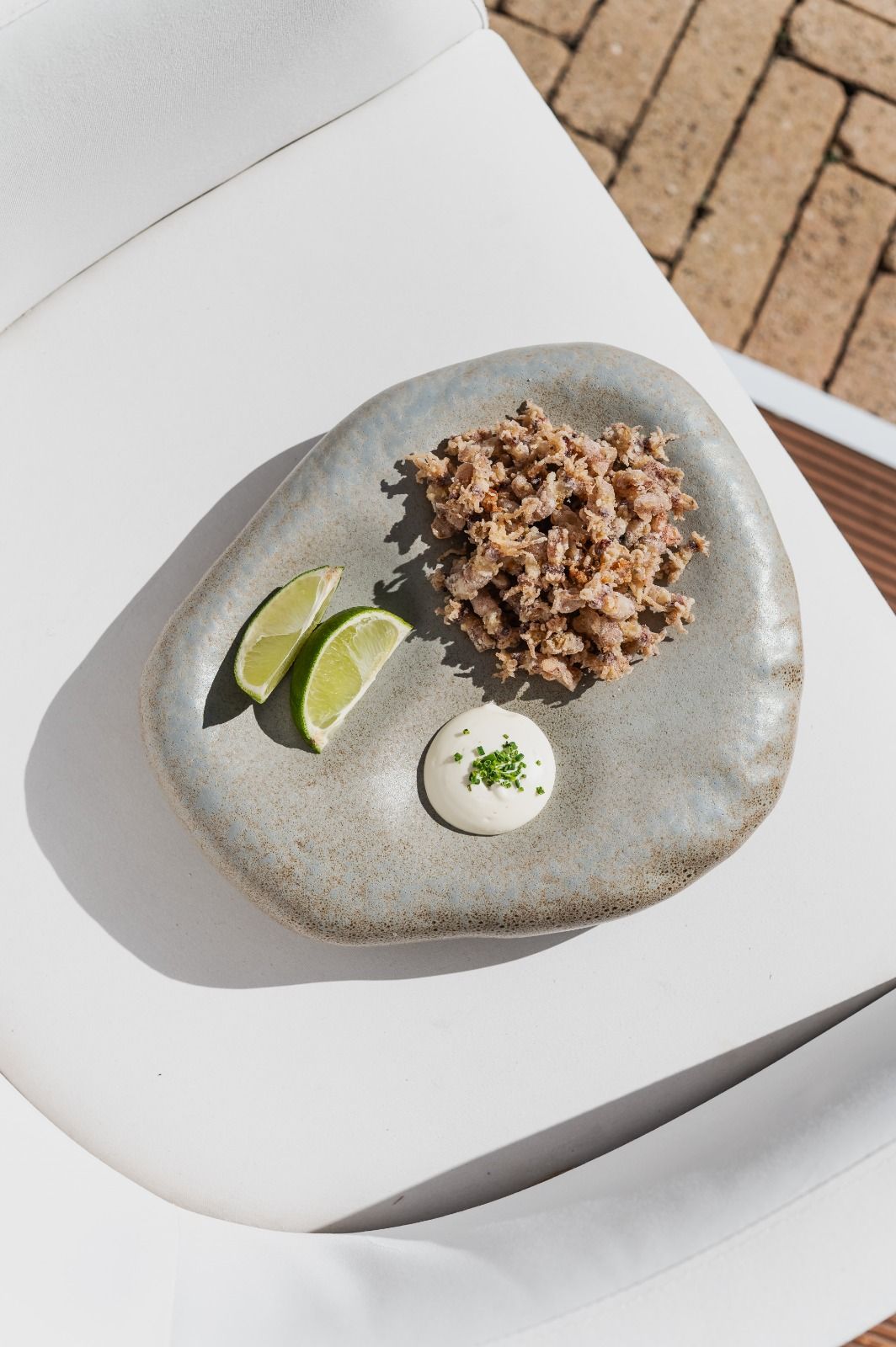 Piatto gourmet impiattato con avocado a fette, salsa cremosa e cereali su un tavolo bianco all'aperto.