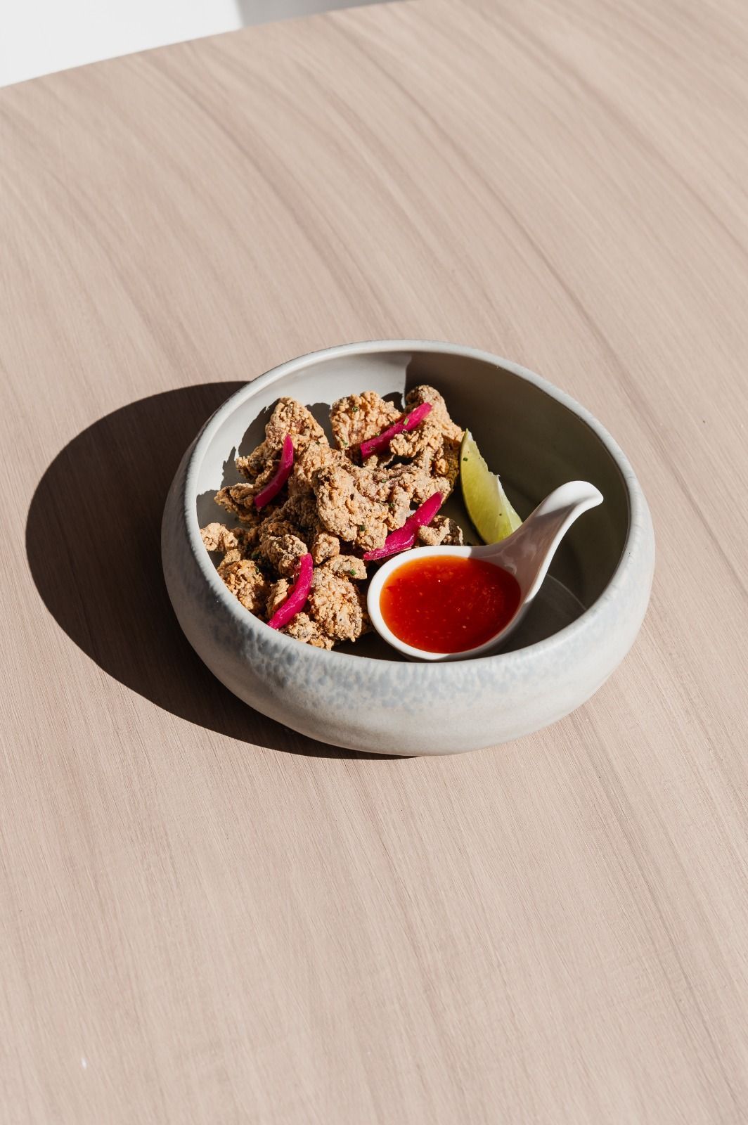 Una ciotolina di granola con frutta e salsa rossa su un tavolino di legno chiaro.