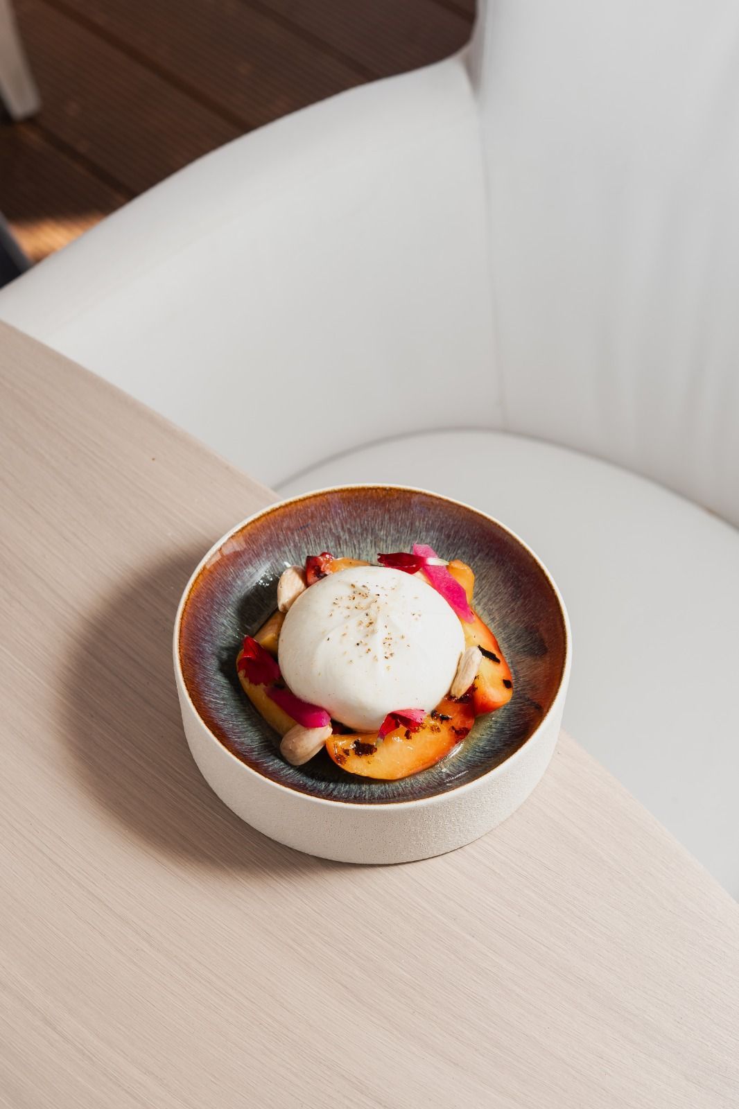 Una ciotola da dessert con una pallina di gelato alla vaniglia, frutta e salsa su un tavolo accanto a una sedia bianca.