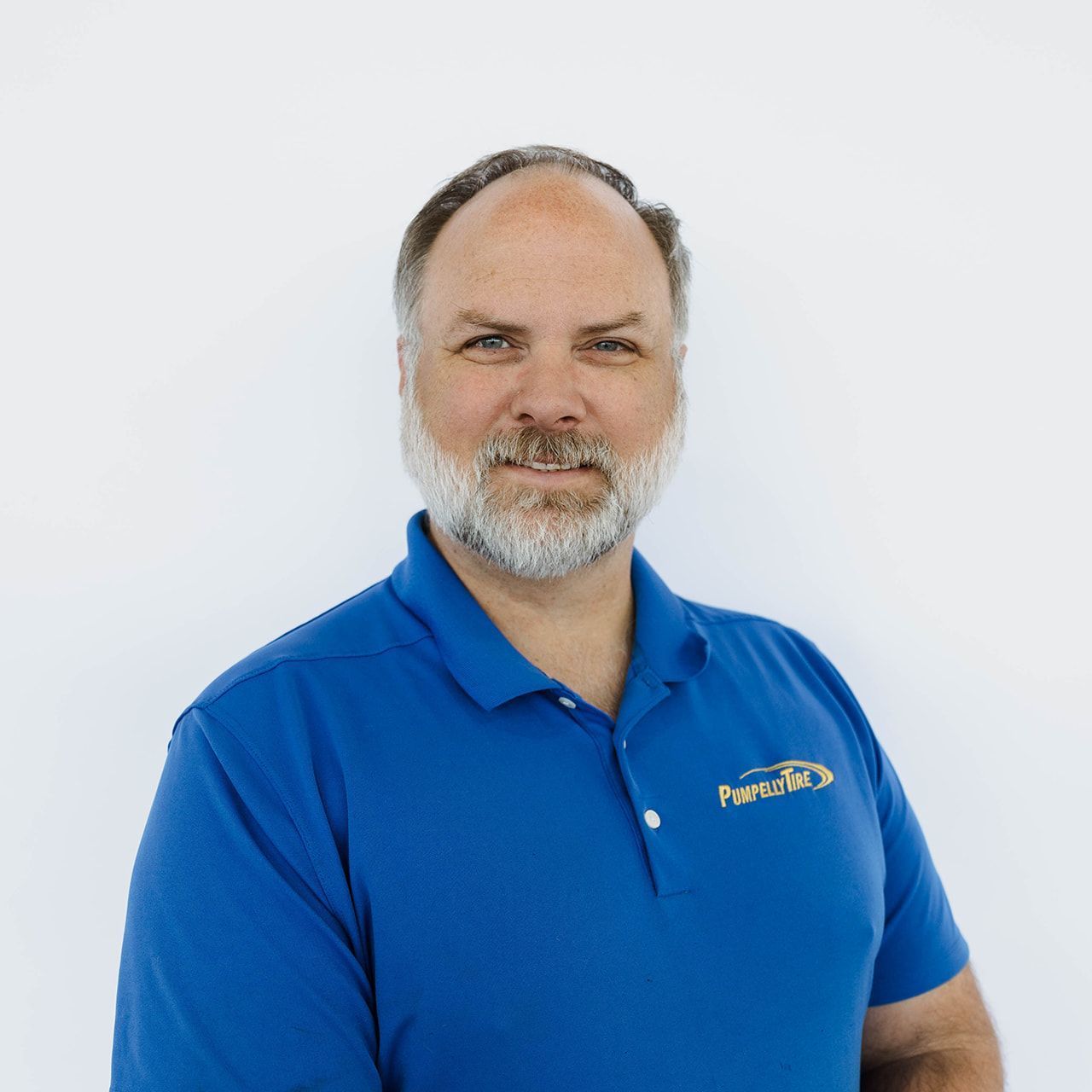 A person with a beard and short hair wearing a blue polo shirt with a company logo, standing against a white background.