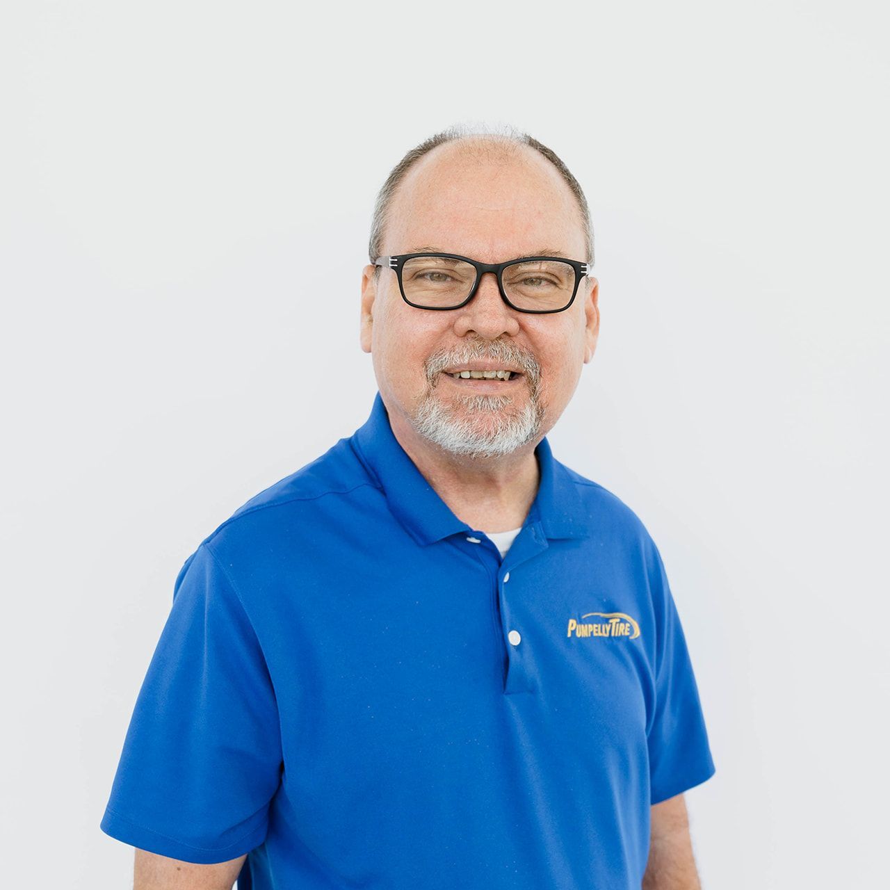 A smiling man with glasses wearing a blue polo shirt with a logo, standing against a plain white background.