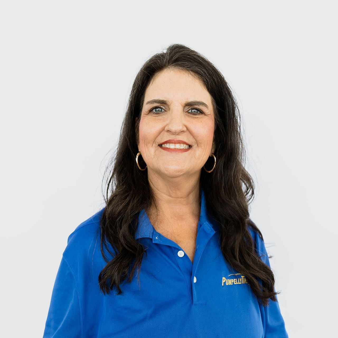 A person with long, dark hair wearing a blue polo shirt, smiling against a plain white background.